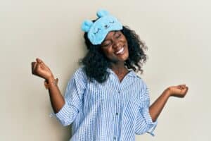Beautiful african young woman wearing sleep mask and pajama very happy and excited doing winner gesture with arms raised, smiling and screaming for success. celebration concept.